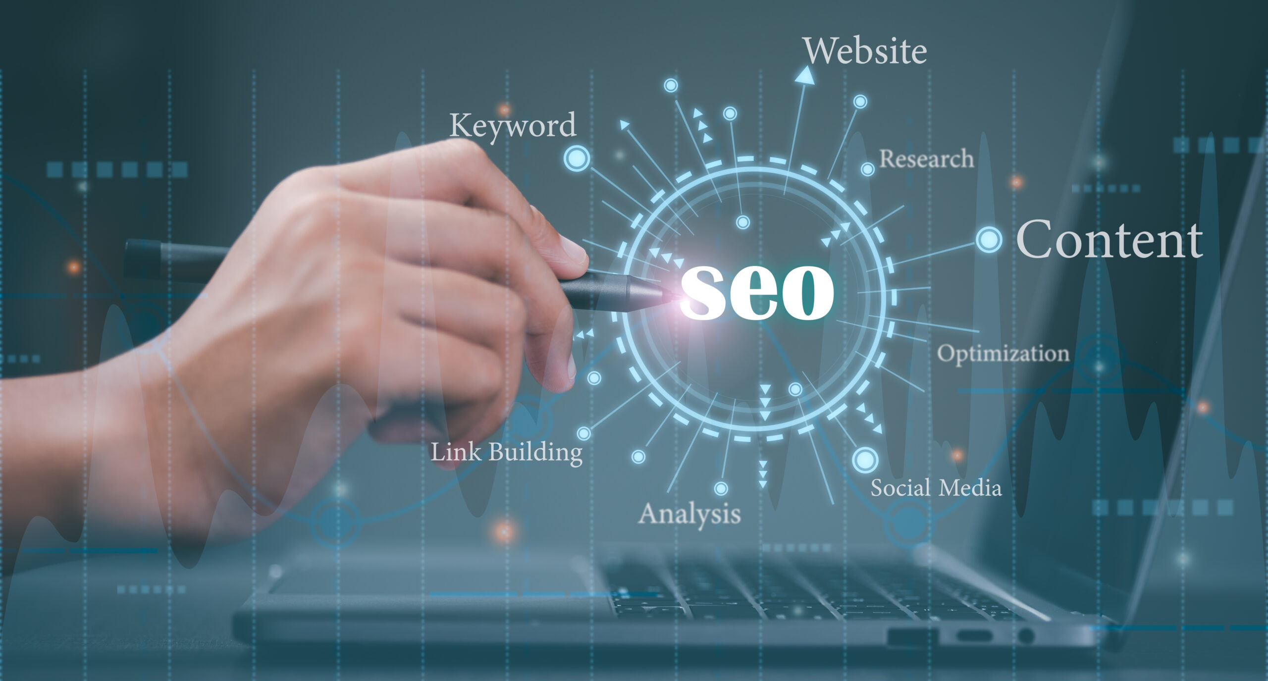 Hand holding a pen pointing at SEO graphic with terms like content, keyword, website, link building, and social media.